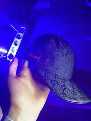 Svart keps med GG-mönster och ränder - Snygg svart keps med ton-i-ton GG-mönster och klassiska gröna och röda ränder på sidan. Böjd skärm och justerbar passform. Perfekt accessoar för en trendig streetwear-look.
