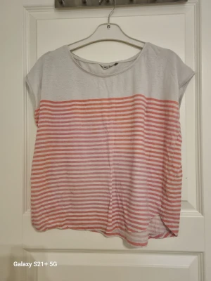 Randig topp i vitt och rosa - Kortärmad topp med ljusgrå överdel och horisontella rosa och vita ränder nedtill. Avslappnad passform och rund halsringning. Perfekt till jeans eller shorts för en chill look.