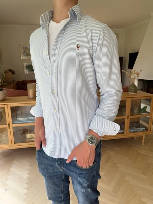 Ralph Lauren skjorta blå/vit randig herr slim fit - Klassisk Ralph Lauren Oxford-skjorta med blåvita ränder och broderad Polo Pony-logga. En tidlös favorit som passar perfekt till jeans, chinos eller under en stickad tröja. Preppy stil när den är som bäst.  #RalphLauren #PoloRalphLauren #Oxford #OxfordShirt #Skjorta #Randig #Blå #Vit #Preppy #OldMoney #QuietLuxury #BusinessCasual #SmartCasual #Designer #Herr #Classic #Polo #Kvalitet #Mode