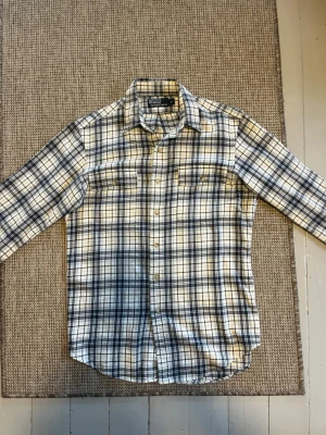 Rutig skjorta från Polo Ralph Lauren - Snygg rutig skjorta från Polo Ralph Lauren i blått och beige. Skjortan har klassisk krage, knäppning framtill och två bröstfickor. Perfekt för en avslappnad men stilren look. Storlek S