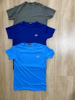 3-pack sport-tshirts Nike & Adidas - Säljer ett 3-pack sportiga t-shirts i olika färger: en grå, en mörkblå från Nike och en ljusblå från Adidas. Alla har rund halsringning och korta ärmar, tillverkade i ett lätt och snabbtorkande material som passar perfekt till träning.