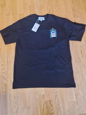 Svart t-shirt med tryck från Casablanca - Svart t-shirt från Casablanca med färgglatt tryck på bröstet som föreställer en byggnad och texten 'Avenida Casablanca'. Klassisk passform och rund halsringning. Perfekt för dig som vill ha en stilren men unik look.