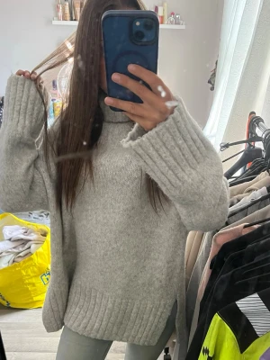 Ljusgrå oversized stickad polotröja  - Mysig ljusgrå stickad polotröja med oversized passform och breda ribbade muddar vid ärmslut och nederkant. Tröjan har hög polokrage och är perfekt för kalla dagar. Materialet ser ut att vara mjukt och värmande, troligen ull- eller ullmix.