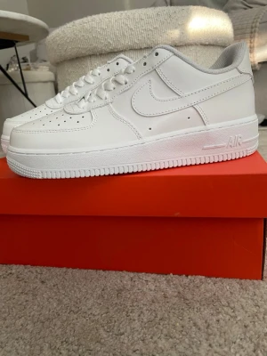 Nike Air Force 1 vita sneakers, strl 41 - Klassiska Nike Air Force 1 sneakers i helvitt läder med perforerad tåbox, vit sula och ikonisk Swoosh på sidan. Skorna har lågt skaft och matchar till det mesta. Perfekta för dig som gillar stilrena och tidlösa sneakers. Lådan ingår inte 
