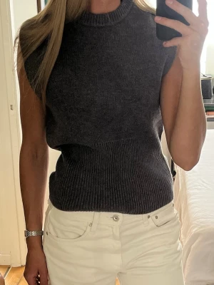 Stickad tröja - Mörkgrå ärmlös stickad tröja med ribbad kant nedtill och vid halsen. Tröjan har en figursydd passform och är perfekt att bära över en skjorta eller t-shirt. Aldrig använd❣️ 