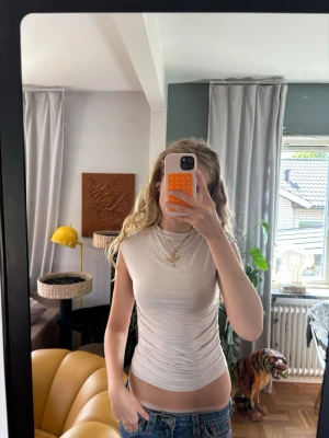 Vit ärmlös ribbad topp - Säljer en vit, tight och ärmlös topp med ribbad struktur och snygg snörning i sidan. Toppen har hög hals och sitter figurnära, perfekt till jeans eller kjol. Enkel men ändå trendig design som passar till många olika stilar.