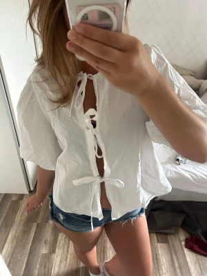 Vit blus med knyt och puffärm - Säljer en luftig vit blus med korta puffärmar och tre knyt framtill. Jag har använt den en gång så den är nästan helt ny! 