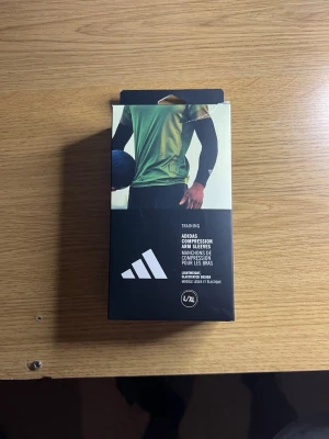 Adidas svarta kompressionsärmar L/XL - Säljer ett par svarta kompressionsärmar från Adidas i storlek L/XL. Perfekta för träning med lätt och elastiskt material som andas. Ärmarna har Adidas-logga och sitter tight för extra stöd under sportaktiviteter.