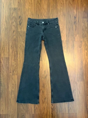 Mörkgråa bootcut jeans med lowwaist - Säljer ett par mörkgråa bootcut jeans med utsvängda ben. Jeansen har lowwaist och dragkedja med knapp framtill.