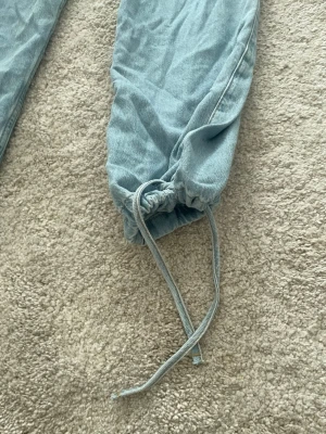 Ljusblå baggy jeans med dragsko - Zara - Prislappar fortfranade på! Byxor från Zara- Säljer ett par ljusblå baggy jeans med dragsko i bensluten. Jeansen har en avslappnad passform och är gjorda i klassiskt denimtyg. Perfekta för en chill och trendig streetwear-look.
