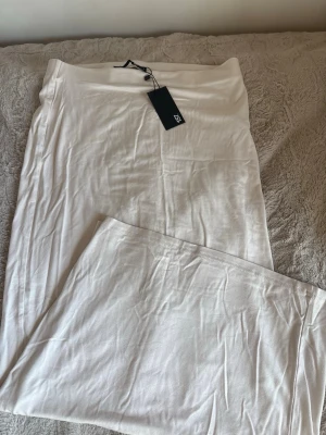 Vit långkjol från 157 i S - Säljer en enkel och stilren vit långkjol från 157. Kjolen har en rak passform och är gjord i ett mjukt och lätt material som känns skönt mot huden. Perfekt att matcha med en crop top eller hoodie för en clean look.