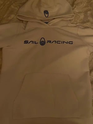Helt ny vit hoodie från Sail Racing - Snygg vit hoodie från Sail Racing med svart logga och text på bröstet. Klassisk känguruficka framtill och huva med tryckt logotyp. Perfekt för en avslappnad och sportig stil. Mjuk bomullskänsla och stilren design. fraktar inom 8h och priset går o diskutera ! 