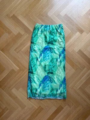 Grönblå långkjol från Gina Tricot - Säljer en midikjol från Gina Tricot med grönt och blått abstrakt mönster. Kjolen har en rak passform och är tillverkad i mjuk polyester, perfekt för dig som vill sticka ut med färg och mönster.
