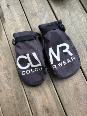 Svarta tumvantar från ColourWear - Svarta tumvantar från ColourWear med stor vit logga på ovansidan. Vantarna har justerbart band vid handleden och elastisk mudd. Materialet är slitstarkt och passar perfekt för kalla dagar.