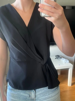 Svart omlottblus med knyt - Omlottblus med knyt i sidan och v-ringad hals. Aldrig använd