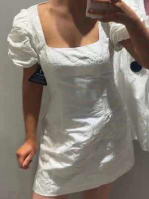Vit kort klänning med puffärm - Säljer en vit kort klänning med fyrkantig ringning och puffärmar. Aldrig andvänt då ja köpte fel storlek. Nypris 499!! Kom privat för fler bilder!!