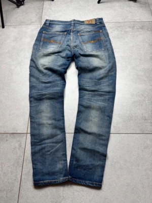 Nudie Jeans regular fit - Säljer ett par klassiska blå jeans från Nudie Jeans med snygg slitning och kontrastsömmar. Jeansen har normal ben, fem fickor och Nudie-loggan på bakfickan. Perfekta för dig som gillar en avslappnad och trendig stil. Skriv privat om du vill ha mer bilder eller mått👌🏼