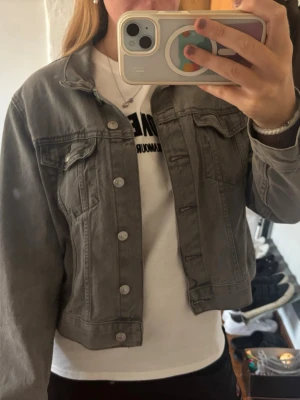 Grå jeansjacka i klassisk modell - Snygg grå jeansjacka i klassisk modell med raka sömmar och silverfärgade knappar. Jackan har två bröstfickor med lock och knapp samt en avslappnad passform. Perfekt att slänga över en t-shirt för en cool vardagslook.