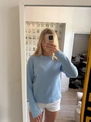 Ljusblå stickad tröja - Mysig ljusblå stickad tröja med rund halsringning och långa ärmar. Tröjan har en enkel, klassisk design med ribbstickade muddar vid ärmslut och nederkant. Perfekt att matcha med jeans eller kjol för en avslappnad look.