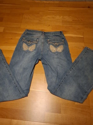 Blå bootcut jeans med broderi - Säljer ett par blå bootcut jeans med snygga broderade fickor bak, dekorerade med silverfärgade detaljer och nitar. Nypris 550-600 vet inte exakt