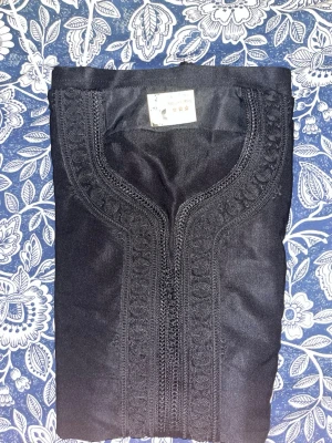 Svart kaftan med broderade detaljer - Säljer en svart kaftan med snygga broderade detaljer längs halsringningen och framtill. Plagget har en rak passform och är tillverkat i ett mjukt tyg som känns bekvämt mot huden. Perfekt för dig som gillar stilrena och unika plagg.