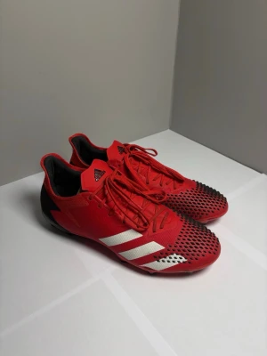Fotbollskor - Adidas Predator 20.2 FG/AG Mutator - Röd/Vit/Svart - Fotbollskor - ADIDAS PREDATOR 20.2 FG/AG MUTATOR - RÖD/VIT/SVART. Skon har FG+AG-dobbar vilket innebär att den kan användas på både naturgräs och konstgräs.  Endast använda 3 gånger så skorna är i princip nyskick. Endast ett fåtal märken vid snörningen. Innersulan och dobbarna ser så gott som nya ut - se bilder. Original lådan ingår inte. Nypris var 1400 kr.  Storlek 42 ⅔ med ett innermått på 27 cm, och passar true to size.  Har du frågor eller undringar så är det bara att höra av dig!