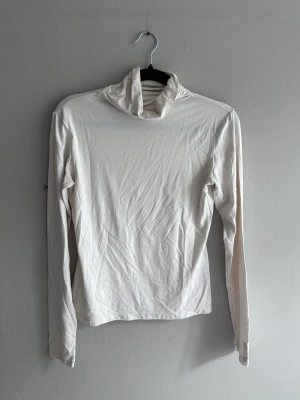 Vit polotröja med långa ärmar - Säljer en enkel och stilren vit polotröja med långa ärmar. Tröjan är i ett mjukt och stretchigt material, perfekt att ha som basplagg eller under en jacka. Passar dig som gillar minimalistisk stil.