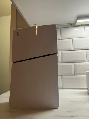 Vit PlayStation 5 Slim konsol - Säljer en PlayStation 5 Slim i stilren vit färg med svart detalj. Konsolen har en modern, kantig design och är tillverkad i plast. Perfekt för dig som vill ha den senaste spelupplevelsen hemma.