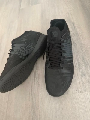 Svarta fotbollsskor från Puma - Säljer ett par helsvarta fotbollsskor från Puma med snygg, diskret design och mönstrad ovandel. Skorna har snörning och greppvänlig sula som passar perfekt för inomhusspel. Materialet är syntet och skon har en modern, slimmad form. Står storlek EUR. 40 men sitter som 38.5