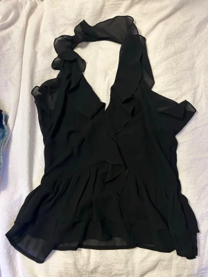 Svart volang topp med omlott - Super fin svart viangtopp topp med en halterneck-ringning. Toppen är ifrån bikbok i ett gott skick🥰🤩