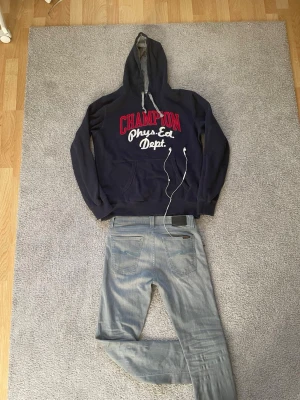 Vintage hoodie  - Mörkblå hoodie från Champion med stor röd och vit text 'CHAMPION Phys. Ed. Dept.' på bröstet. Klassisk känguruficka framtill, dragsko i huvan och mjukt material på insidan. Perfekt för en laidback, vintage look. Storlek = Large. 