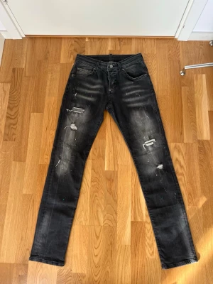 Svarta slitna jeans från Dsquared2 - Säljer ett par svarta jeans från Dsquared2 med slitningar och färgstänk för en cool, trendig look. Jeansen har smal passform, klassisk femficksdesign och knappgylf. Perfekta för dig som gillar streetstyle och vill sticka ut. Hör av er om ni är intresserade eller har några frågor!