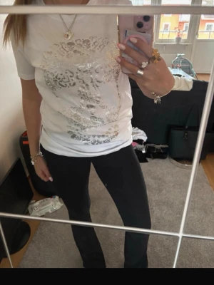 Vit t-shirt med silvertryck - Säljer en vit t-shirt med glansigt silvermönsterT-shirten har korta ärmar och en klassisk passform. Perfekt för dig som gillar detaljer som sticker ut.