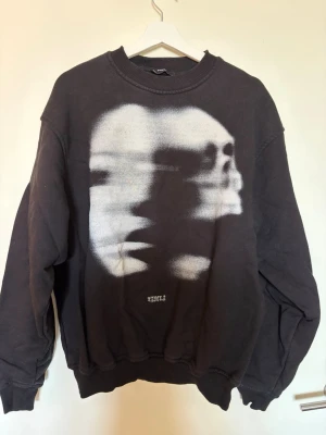 Svart sweatshirt Favela M - Svart sweatshirt med stort grafiskt ansikte i vitt på framsidan. Tröjan har rund hals, ribbade muddar och avslappnad passform. Sitter lite oversized.