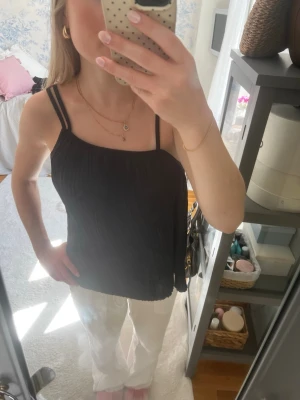 Svart plisserad linnetopp - Snygg svart linnetopp med tunna axelband och plisserat tyg. Toppen har en lös passform och är perfekt för en trendig och avslappnad look. Enkel att matcha med både jeans och kjol.