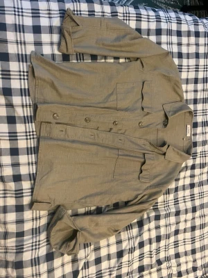 Olivgrön overshirt med fickor från Sandö - Stilren olivgrön overshirt med två bröstfickor och knäppning framtill. Skjortan har klassisk krage och långa ärmar, perfekt att bära öppen eller stängd. Materialet känns lätt och passar bra till lager-på-lager-stil.