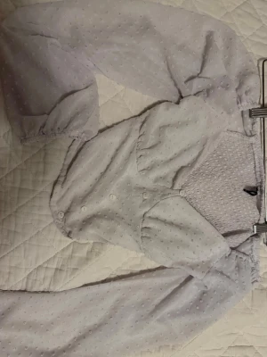 Vit blus med puffiga ärmar - Trendig vit blus med små prickar, puffiga långärmar och smockad rygg. Knappar framtill och elastiska ärmslut ger en söt och modern siluett. Perfekt för dig som gillar en feminin och stilren look. Storlek Small