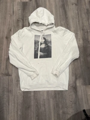 The coo elephant - Snygg vit hoodie med huva och dragsko, prydd med ett stort svartvitt Mona Lisa-tryck på bröstet. Mjuk bomullskänsla och ribbade muddar vid ärmslut och nederkant. 