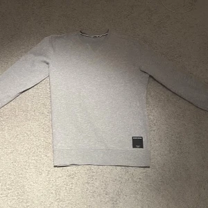 Grå sweatshirt från Björn Borg - Klassisk grå sweatshirt från Björn Borg med rund halsringning och ribbade muddar. Tröjan har en diskret svart patch med logga nertill och är tillverkad i mjukt bomullsmaterial. Perfekt för en avslappnad och stilren look.säljer för 200 kr kan möjligtvis gå med på priser ner till 120 kr!