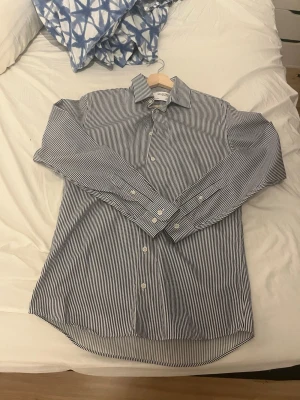 Gråta dig skjorta med knappar från selected homme - Klassisk skjorta med smala grå  och vita ränder, långärmad och med knäppning framtill. Skjortan har en normal passform ochr perfekt för en clean och stilren look.