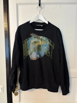 Weekday Sweatshirt - Cool svart sweatshirt med tryck av en örn och texten 'DISCONNECT' i stora bokstäver över bröstet. Tröjan har rund hals, långa ärmar och ribbade muddar vid ärmslut och nederkant. Perfekt för en avslappnad streetwear-look.