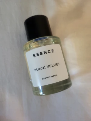 Essnce Black Velvet Eau de Parfum - Essnce Black Velvet Eau de Parfum i en stilren, rund glasflaska med svart lock och vit etikett. Parfymen har en transparent vätska och en modern design som passar perfekt på parfymhyllan.