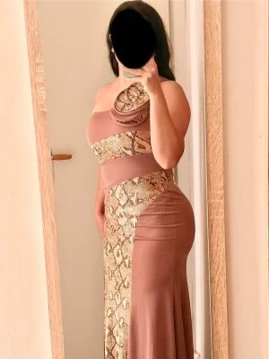 Beige långklänning med ormmönster - Säljer en unik beige långklänning med ormmönstrade detaljer och oneshoulder-design. Klänningen har en asymmetrisk skärning och mjukt, följsamt material som ger en snygg siluett. Perfekt för dig som vill sticka ut med en trendig look. Använd 1 gång på en fest. Helt ny och fint 