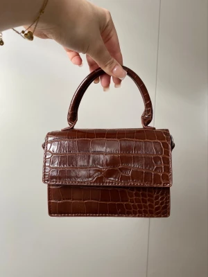 Brun mini handväska i nyskick - Supergullig jacquemus-inspirerad mini handväska i från Monki. Använd 1-2 gånger så den är i nyskick🤍Väskan har ett långt band som går att ta av och ett litet handtag. 