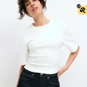 Vit croppad topp från Ginatricot  - Säljer en stilren vit croppad topp från Ginatricot med rund halsringning och korta, vida ärmar. Toppen har en enkel och clean look som passar perfekt till jeans eller kjol. Materialet känns mjukt och har en lätt stretch för skön passform. Använt 2 gånger