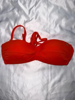 Orange bikini set  - Bikini i två delar. Överdelen är en bandeau-modell med knytning bak och underdelen är en trosa med ränder i midjan.