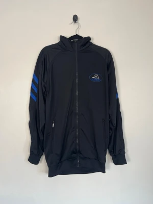 Vintage Adidas Track Jacket Svart Grå Blå XL Träningsjacka Zip-Up Y2K - • Storlek: XL • Färg: Svart, grå och blå • Passform: Regular Fit  • Krage: Hög ståkrage med dragkedja • Material: 100 % polyester  Skick: Plagget är i väldigt fint skick. Eventuella anmärkningar anges alltid tydligt i beskrivningen och visas på bilderna.  Nypris: Cirka 1 000 kr.  📦 Skickas snabbt och packas omsorgsfullt. 💬 Hör gärna av dig om du har frågor eller vill se fler bilder. 🤝 Samfrakt erbjuds vid köp av flera plagg – kika gärna in mina andra annonser!