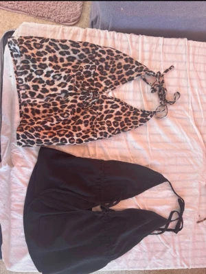 Leopardmönstrad och svart halterneck topp - Två snygga halterneck toppar, en i leopardmönster och en i svart. Båda har knyt i nacken och är ärmlösa med croppad passform. Perfekta för sommaren och ger en trendig vibe till din outfit. ⚠️OBS!⚠️ du kan köpa båda för 100kr eller en för 55kr!