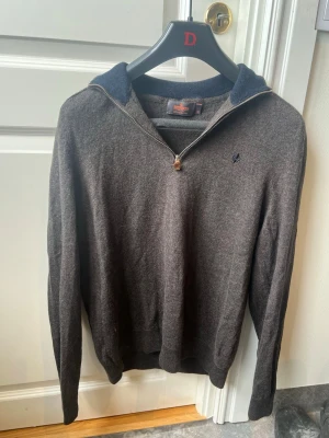 Mörkgrå halvzip-tröja från Morris (har krympt till S) - Mörkgrå stickad tröja från Morris i 100% lammull. Tröjan har halvzip med metallblixtlås, hög krage i mörkare nyans och diskret broderad logga på bröstet. Perfekt för lager på lager och en stilren looks.