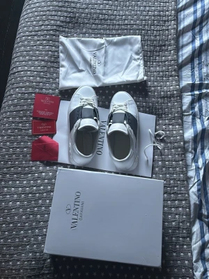 vita sneakers med mörkblå detaljer  - Säljer ett par vita sneakers med mörkblå detaljer med bred mörkblå rem över mitten och vita snören. Skorna har en chunky sula med nitar längs kanten och är tillverkade i slätt läder. Klassisk och stilren design med logga på tungan. Skorna är använd några gånger så lite smutsig och lite creasad.